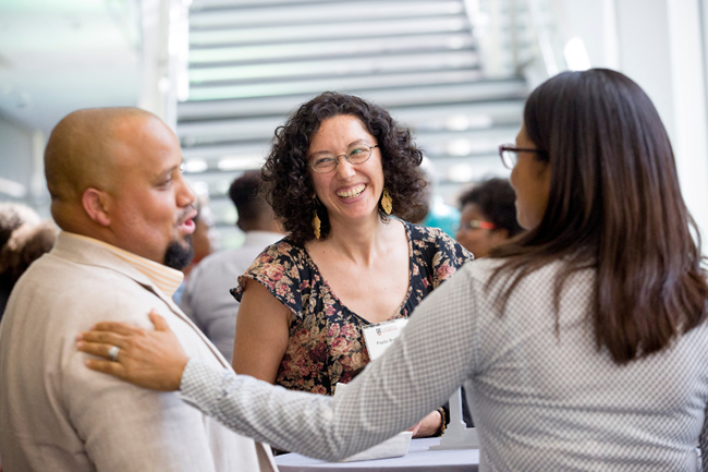 Three faculty members are facing each other, smiling and talking.