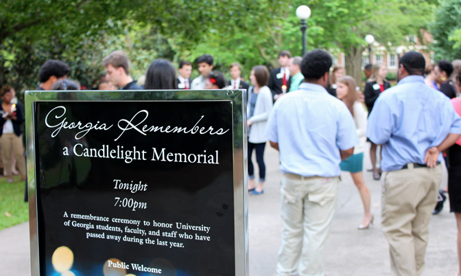 Two men in blue shirts and khaki pants are standing in front of the Georgia Remembers: A Candlelight Memorial sign